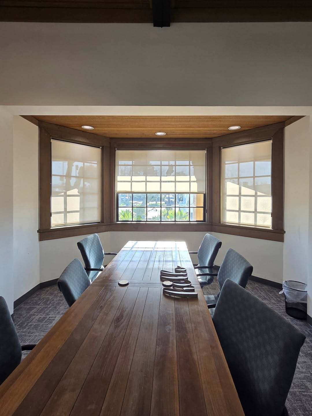Conference room bay window fitted with custom light-filtering roller shades installed by Elite Blinds